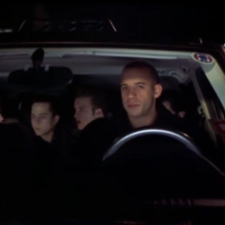Vin Diesel is driving a car with few people in it.